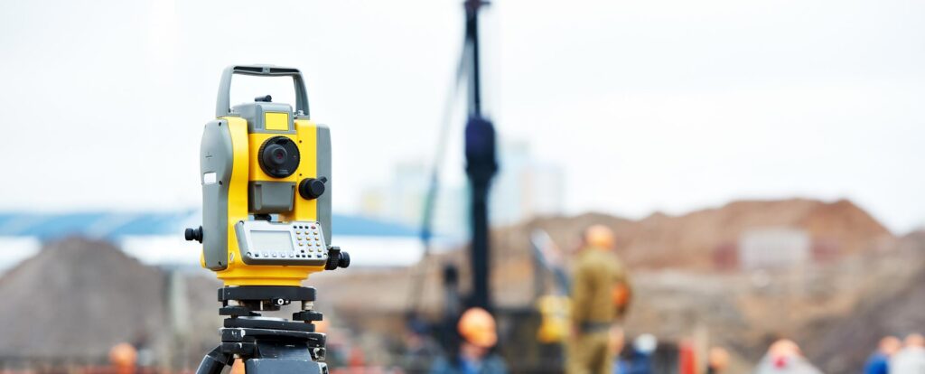 Surveyor's tool in the foreground with a construction site in the background.