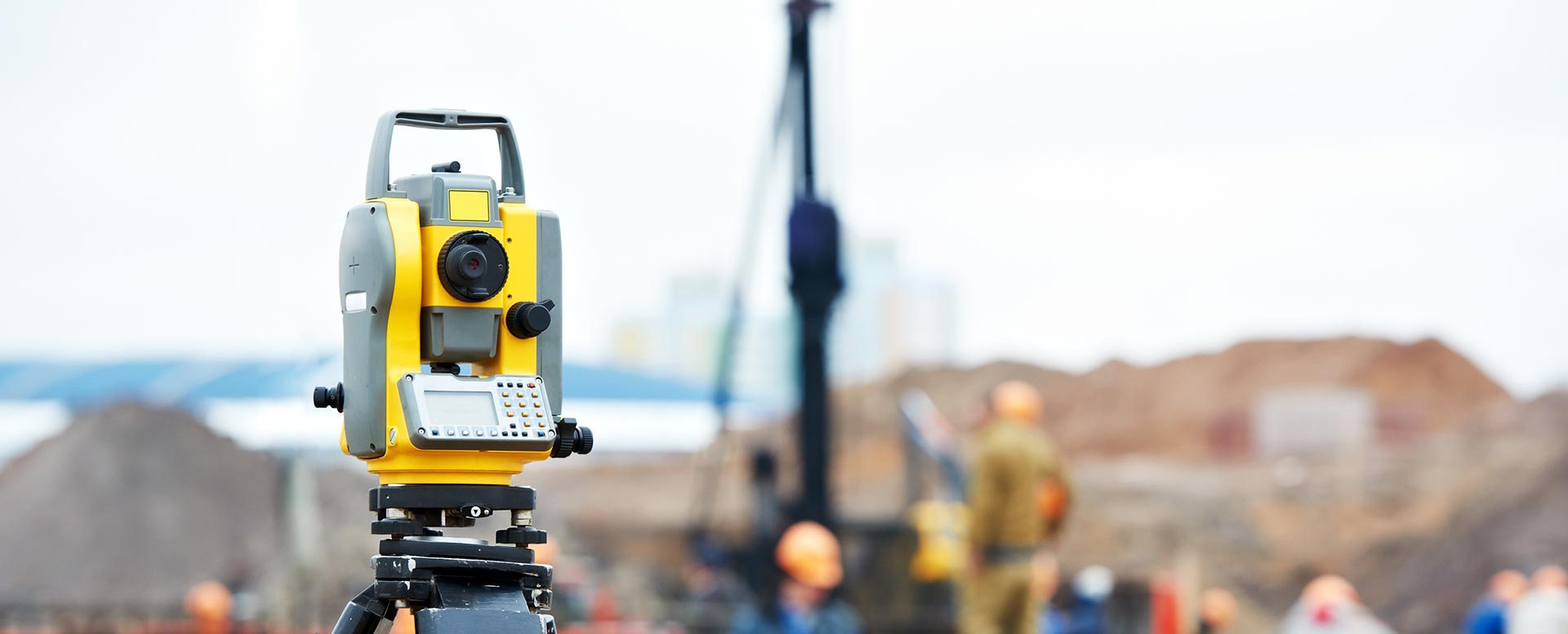 Surveyor's tool in the foreground with a construction site in the background.