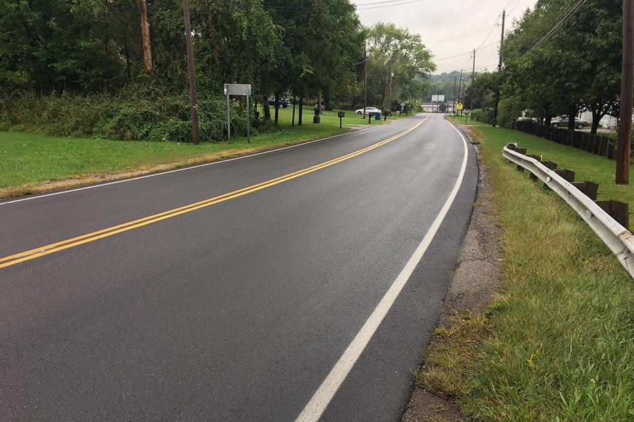 Asphalt road with a double yellow line and a guard rail on one side.