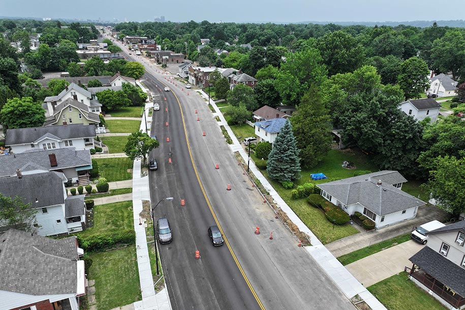 Aerial view of a four lane street with houses on either side and traffic cones in the lanes.