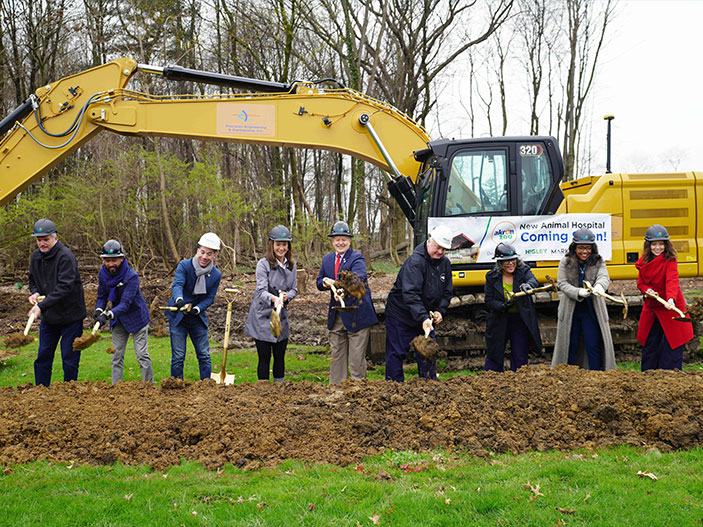Group of people breaking ground with hard hats and shovels.