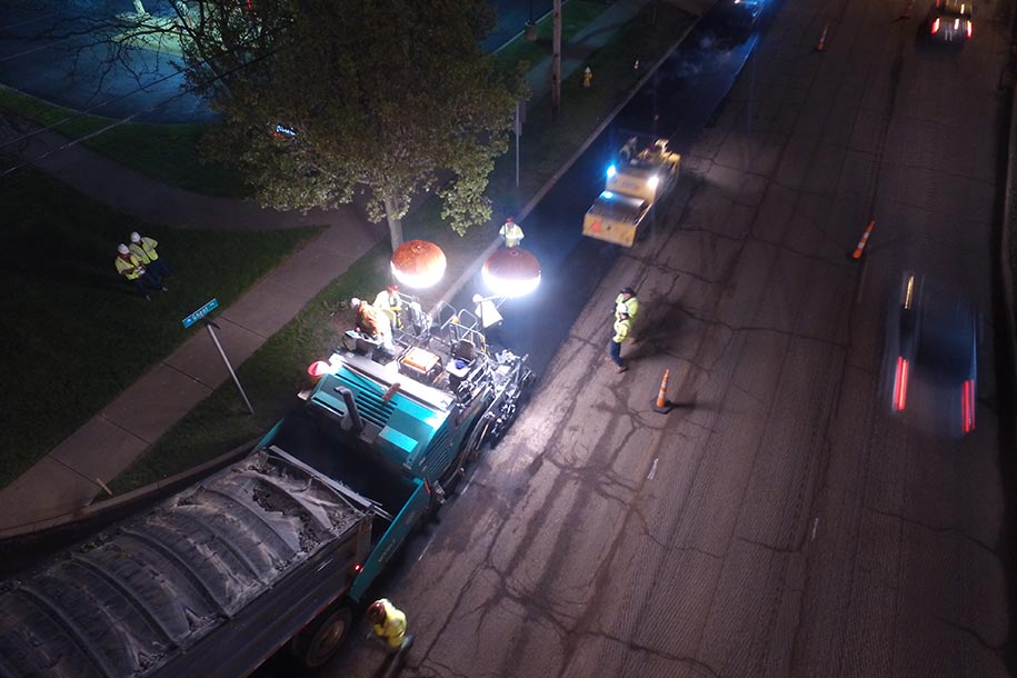 Road crews laying asphalt in the dark with lights helping them to see.