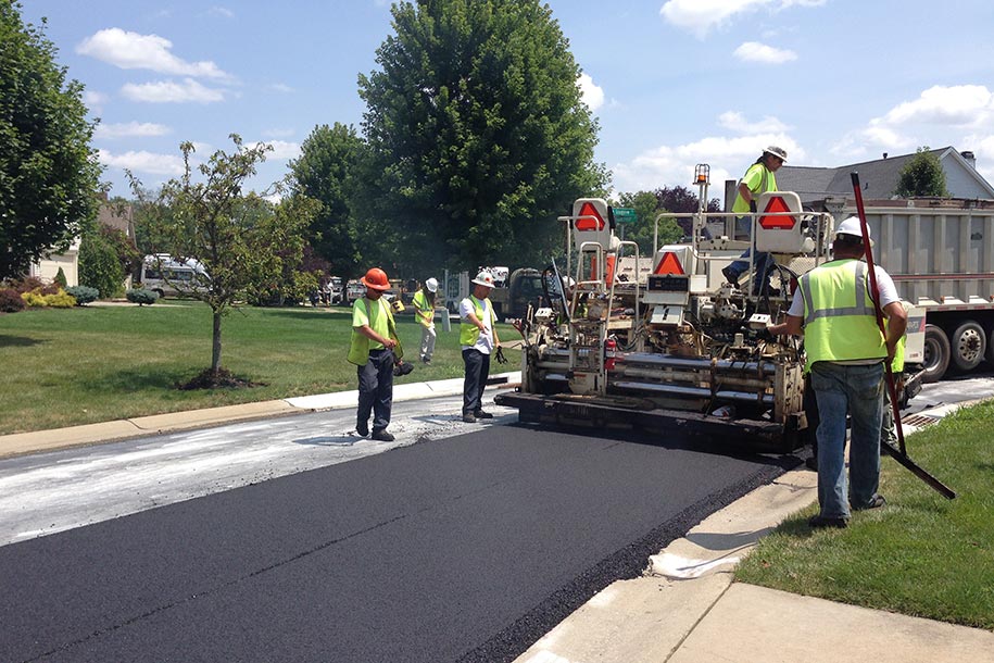 Crew of road workers in neon vests and hard hats laying a new asphalt road.