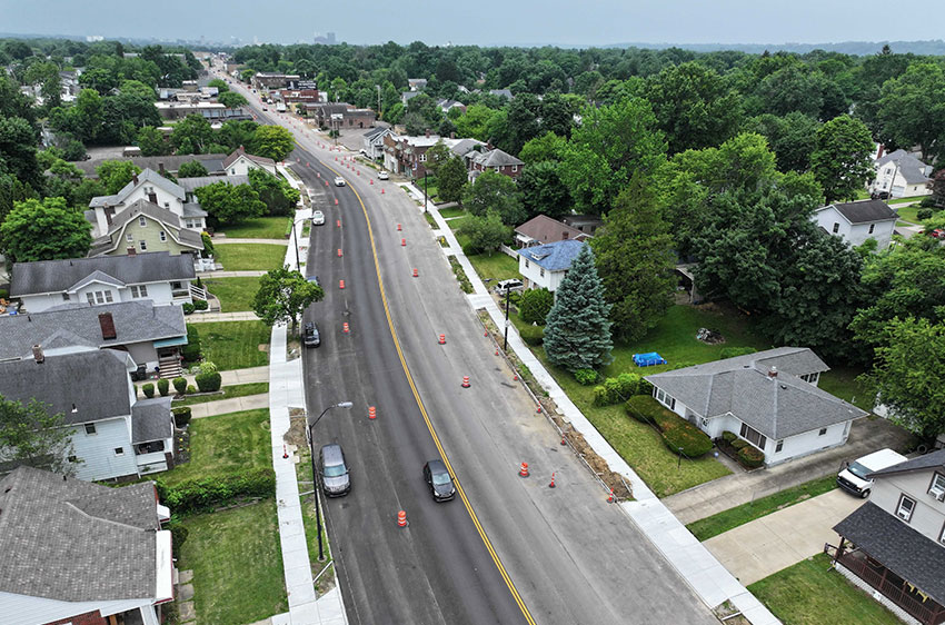 Aerial view of a four lane street with houses on either side and traffic cones in the lanes.