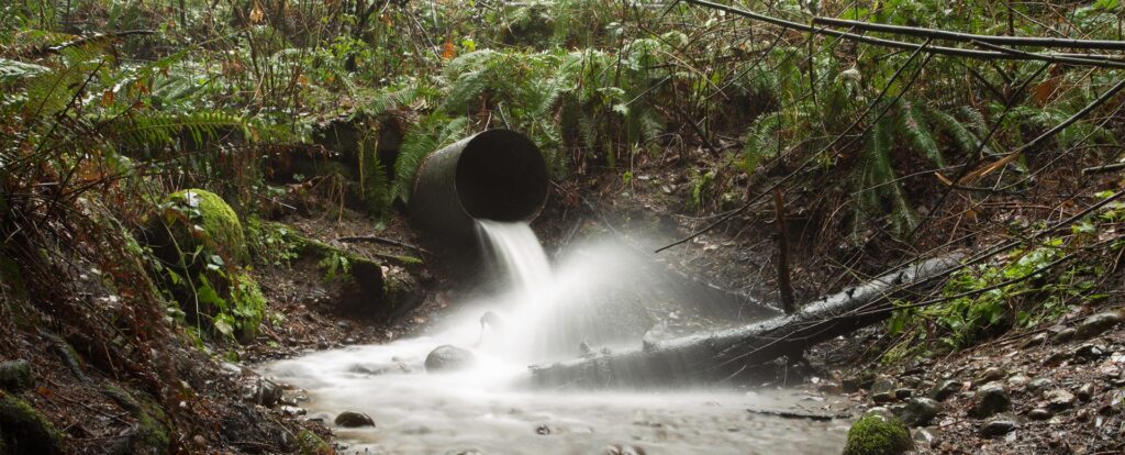 Water flowing from a storm sewer pipe and splashing onto a log.