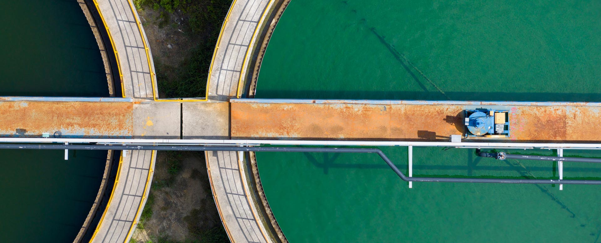 Aerial view of a water treatment facility with circular clarifiers and a maintenance walkway over treatment tanks.