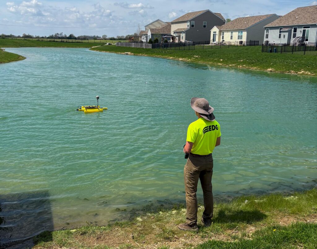 Man in a neon shirt and bucket hat, operating a floating surveying tool