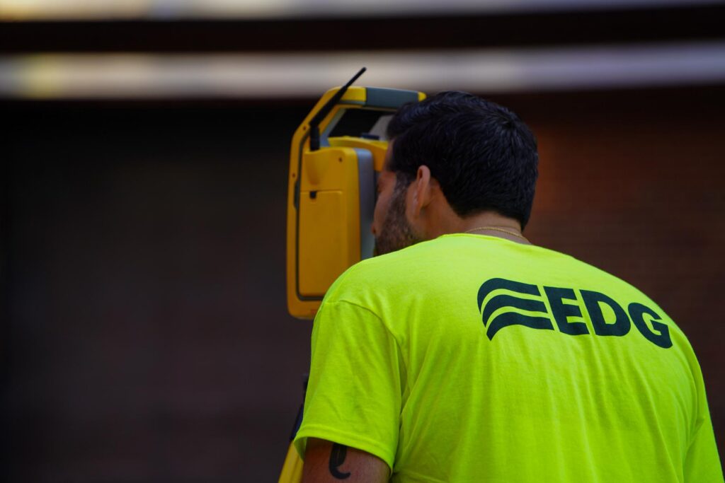 Man in a neon shirt peering through a surveying tool