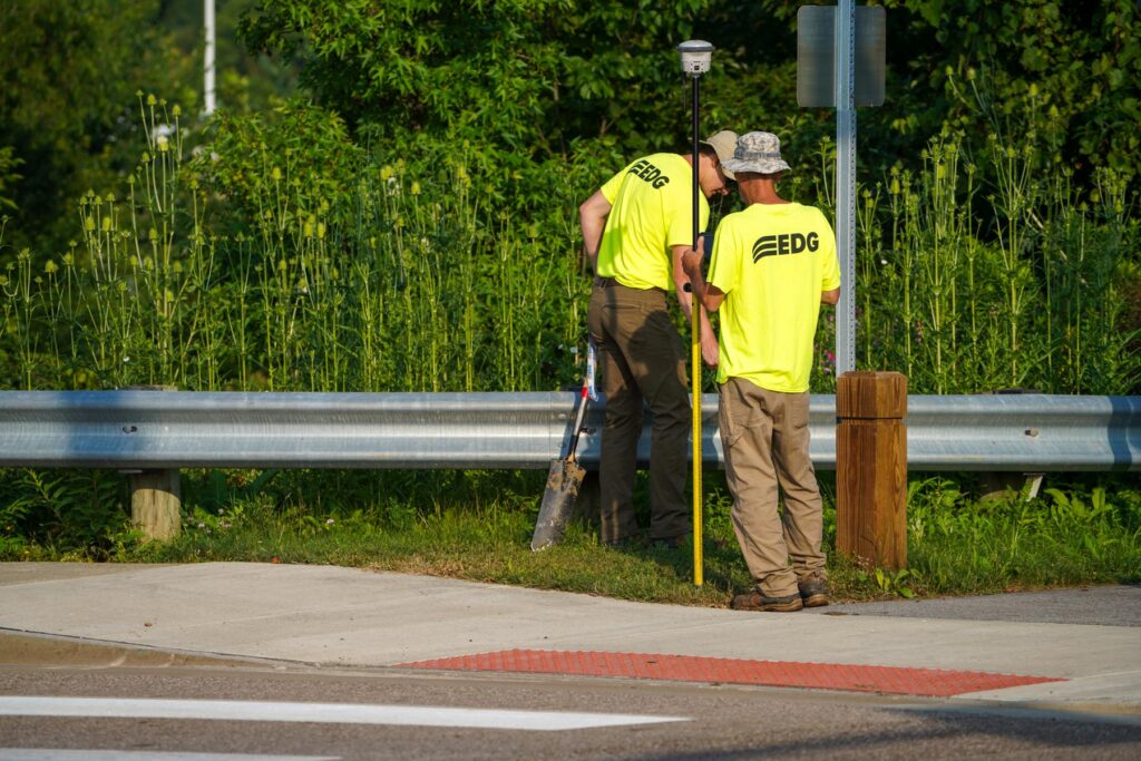 Two men in neon EDG shirts surveying near the road