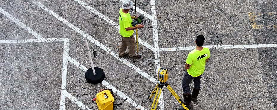 Two men wearing neon shirts, surveying from a parking lot