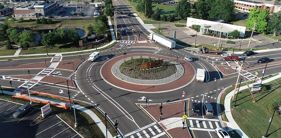 Aerial view of a modern multi-lane roundabout in Green, Ohio, with marked lanes, pedestrian crosswalks, and landscaped center island, surrounded by commercial buildings, parking lots, and vehicles navigating the intersection.